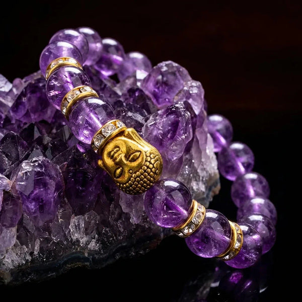 Close-up of amethyst beads and gold Buddha charm on a raw amethyst crystal cluster