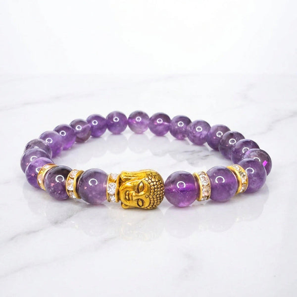 Natural amethyst bracelet with gold Buddha head laid flat on white marble for calm and focus
