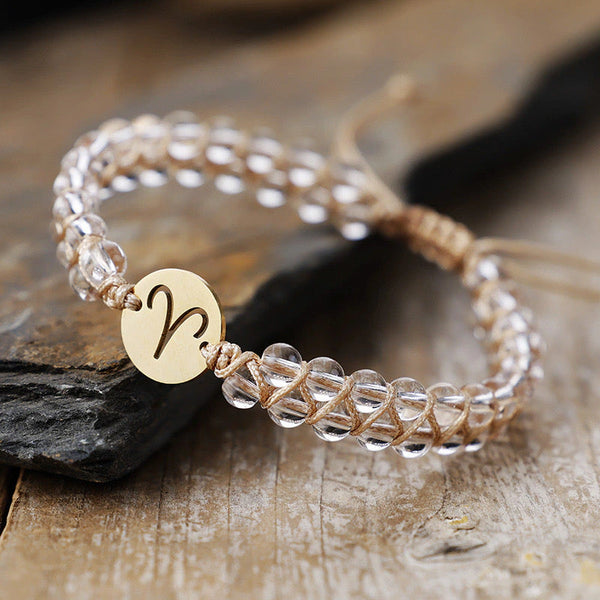 Close-up of the Aries zodiac stone bracelet on slate showing clear quartz beads and engraved gold sign charm