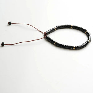 Black onyx protection bracelet with brass accent beads on adjustable braided cord, flat view