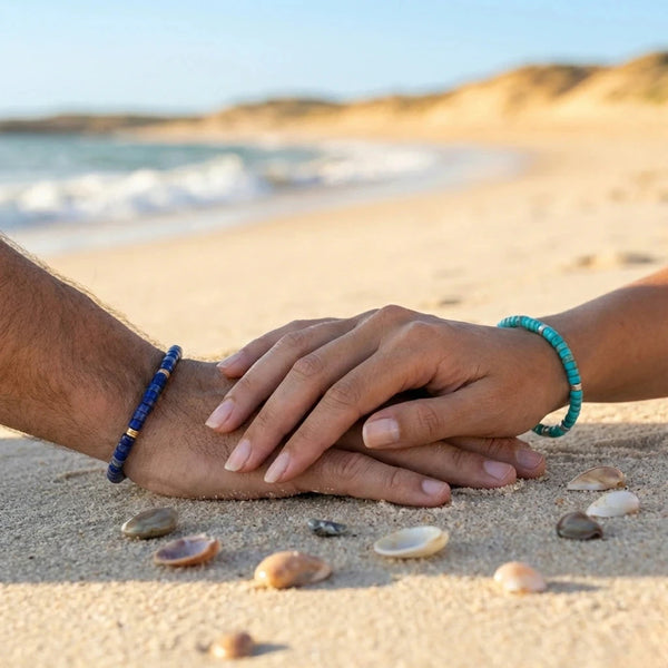 Couple resting hands on sand with seashells wearing the lapis lazuli and imperial jasper bracelets