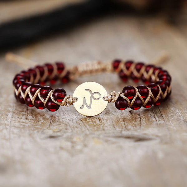 Close-up of the Capricorn zodiac stone bracelet on wood showing deep red garnet beads and engraved gold sign charm