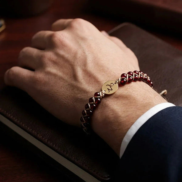 Capricorn zodiac stone bracelet worn on a mans wrist over a leather journal, garnet beads and gold Capricorn charm