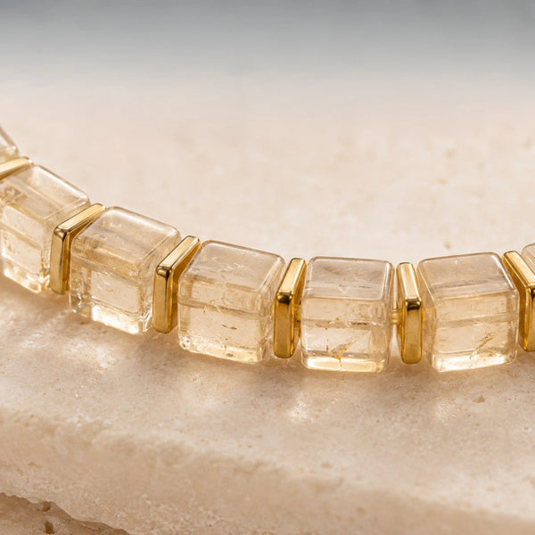 Close-up of translucent citrine cube beads with slim gold hematite spacers on pale stone