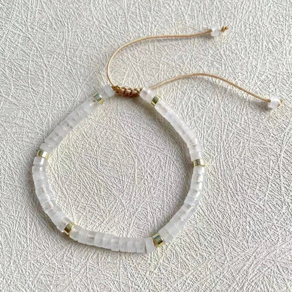 Flat-lay of the clear quartz beaded bracelet with adjustable cord on a textured white surface