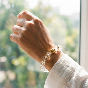 Man wearing clear quartz Sphatik bracelet by a window, gold Buddha bead catching light