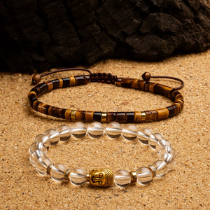 Tiger eye and clear quartz bracelet pair with gold Buddha bead arranged on sand for confidence and clarity