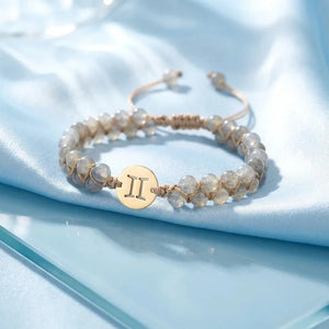 Gemini zodiac energy stone bracelet on blue satin with gold sign charm and adjustable cord, flat-lay view