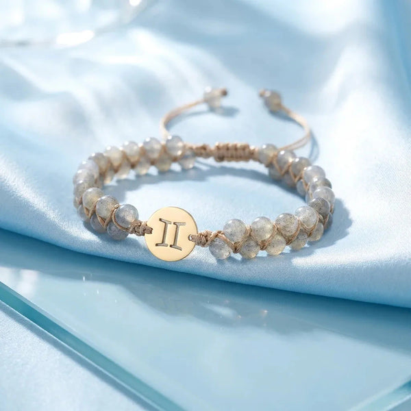 Gemini zodiac energy stone bracelet on blue satin with gold sign charm and adjustable cord, flat-lay view
