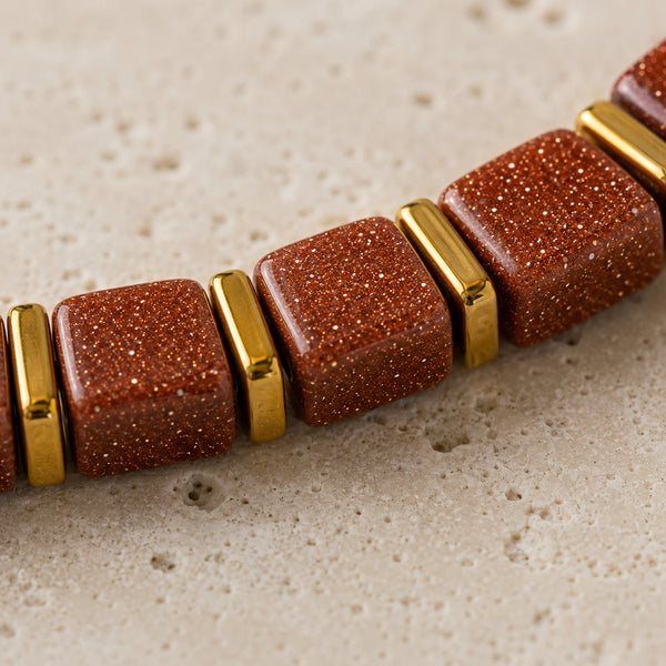 Close-up of shimmering goldstone cube beads with gold spacers showing copper glitter texture