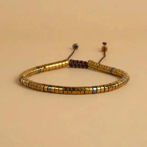 Gold hematite disc-bead bracelet flat on beige with braided adjustable cord for everyday protection
