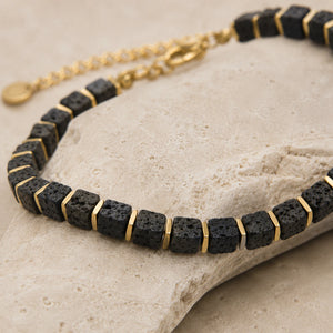 Lava stone bracelet draped over a travertine stone edge showing porous beads and gold spacers