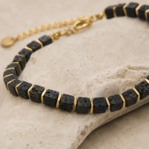 Lava stone bracelet draped over a travertine stone edge showing porous beads and gold spacers