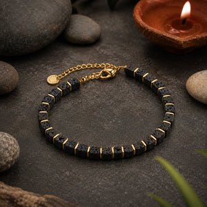 Lava stone bracelet flat lay with a lit diya lamp and smooth pebbles on slate