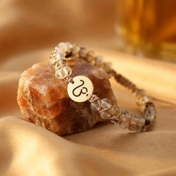Leo zodiac energy stone bracelet resting on a raw crystal over golden satin with gold sign charm, flat-lay view