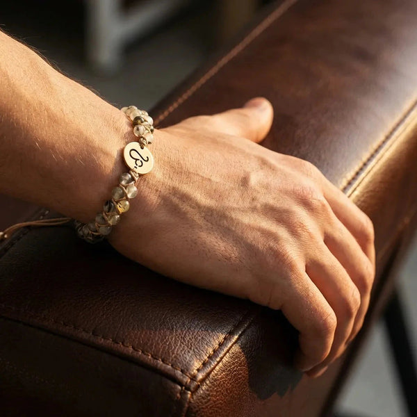 Leo zodiac stone bracelet worn on a mans wrist resting on leather, green prehnite beads and gold Leo charm
