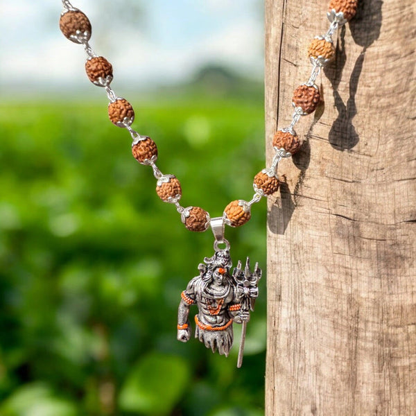 Lord Shiva pendant and rudraksha mala with silver caps styled on wood against green fields