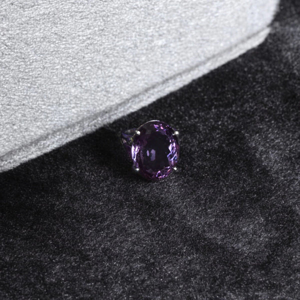 Faceted purple amethyst ring resting on soft grey and black felt in gentle light