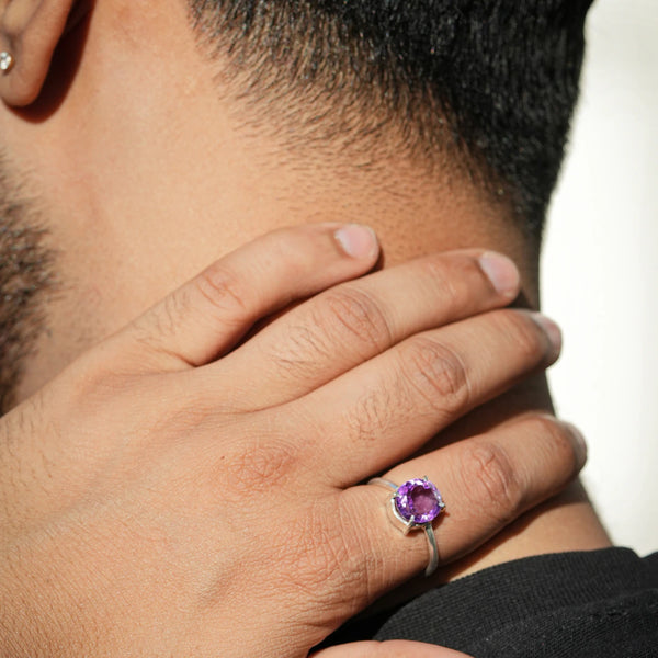 Purple amethyst ring worn on a hand held near the face in natural sunlight
