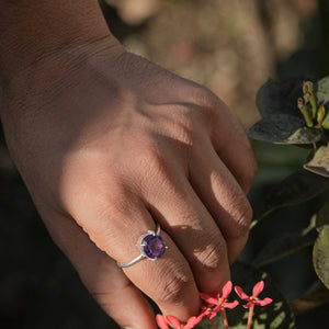 Amethyst ring worn on a finger in daylight beside blooming flowers