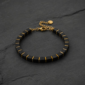 Black onyx bracelet with golden hematite laid on dark slate, adjustable gold chain and clasp visible