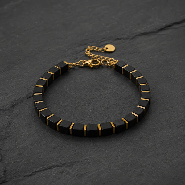 Black onyx bracelet with golden hematite laid on dark slate, adjustable gold chain and clasp visible
