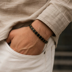 Black onyx bracelet with golden hematite worn on a man's wrist, matte black cube beads with gold spacers