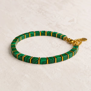 Malachite bracelet with square green beads and gold spacers laid flat on a cream stone surface