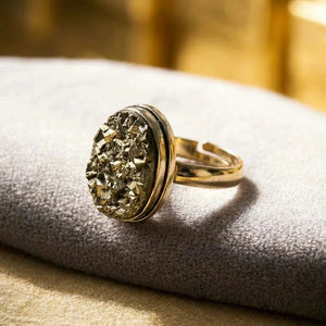 Golden druzy pyrite ring with a gold-toned band resting on a grey velvet cushion