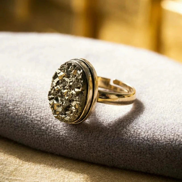 Golden druzy pyrite ring with a gold-toned band resting on a grey velvet cushion