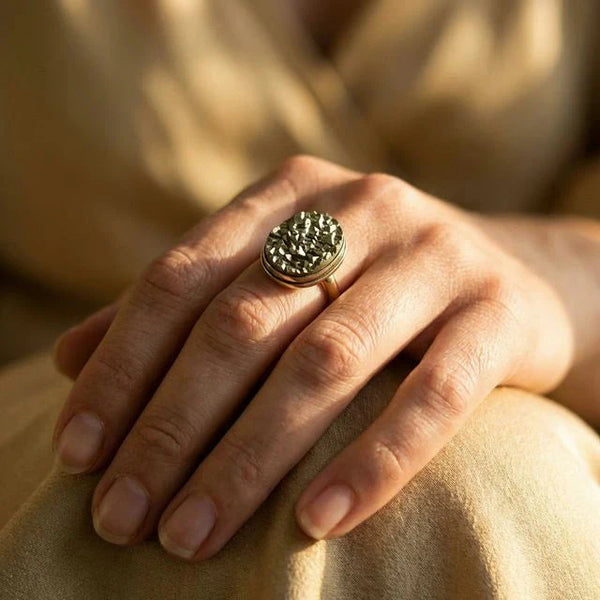 Pyrite stone ring worn on the finger against warm beige clothing in soft light