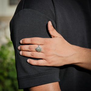 Pyrite ring worn on a hand resting on the arm outdoors with green foliage behind