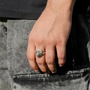 Raw pyrite ring worn on a man's hand beside washed denim in bright sunlight