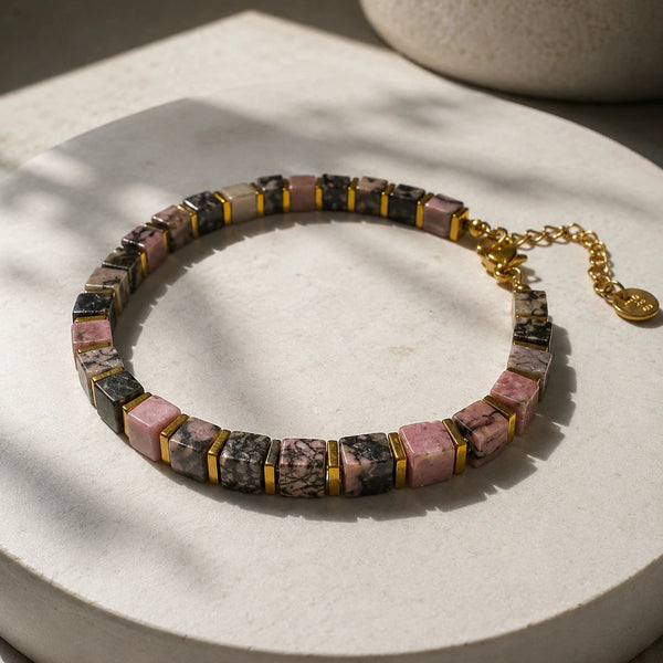 Rhodonite and golden hematite bracelet laid flat on a cream pedestal in soft light
