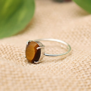 Tiger eye stone ring in silver prong setting resting on woven fabric, side angle