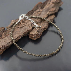 Close-up of faceted pyrite bead wealth anklet on bark showing golden metallic sheen