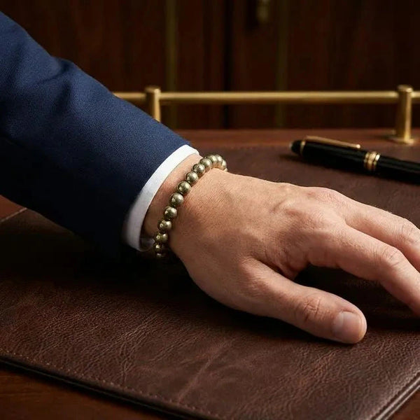 Round pyrite wealth bracelet worn on a man's wrist with a navy suit at a desk