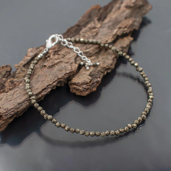 Raw pyrite bead anklet with silver clasp draped over driftwood bark