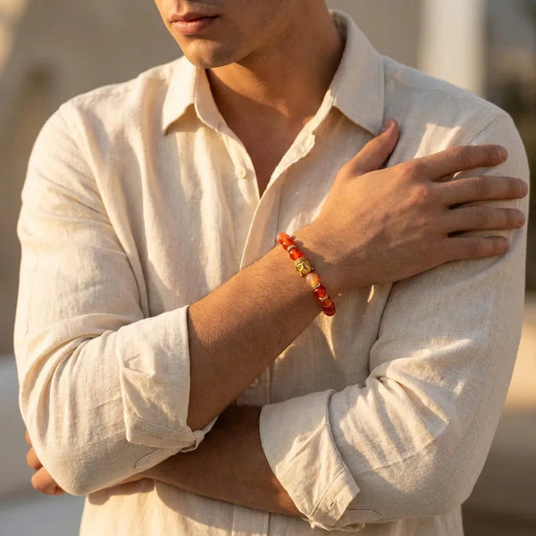 Man wearing red carnelian bracelet outdoors in warm light, gold Buddha bead on wrist