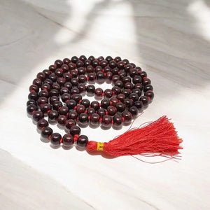 Red sandalwood meditation mala with 108 beads and red tassel on marble, front view