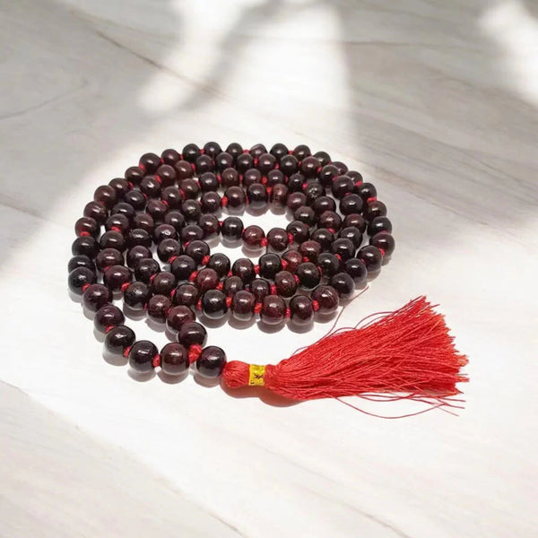 Red sandalwood meditation mala with 108 beads and red tassel on marble, front view