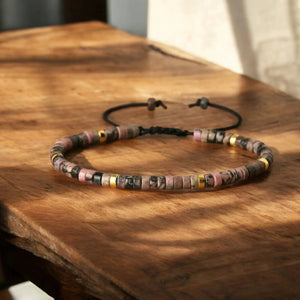 Pink and black rhodonite bracelet with gold spacers on a wooden table for compassion