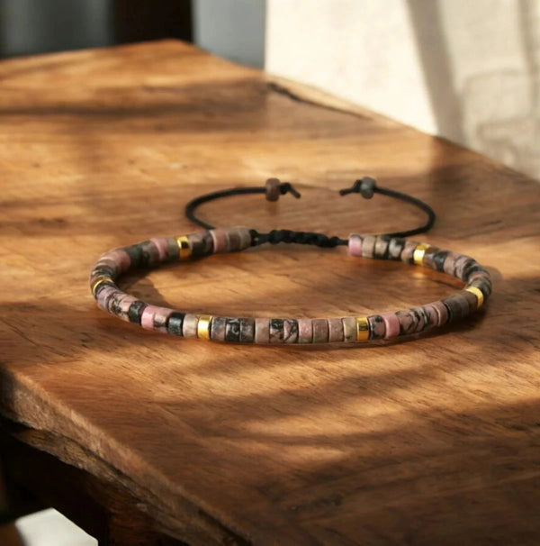 Pink and black rhodonite bracelet with gold spacers on a wooden table for compassion