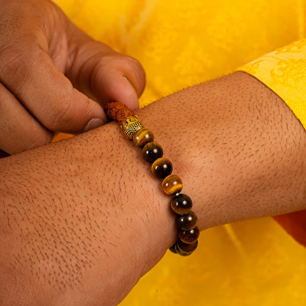 Close-up of rudraksha seed, tiger eye and gold Buddha beads on wrist against a yellow backdrop