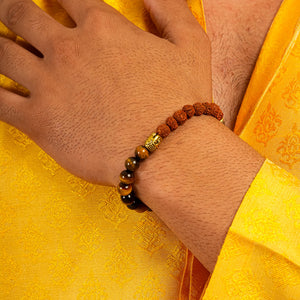 Rudraksha and tiger eye bracelet worn on wrist over yellow silk showing gold Buddha bead accent