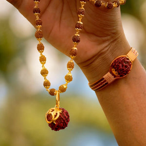 Om Shree gold pendant on rudraksha necklace held up outdoors with copper rudraksha bracelet on wrist