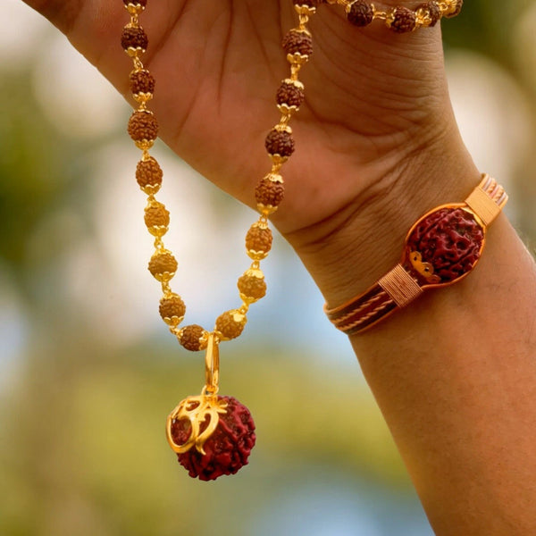 Om Shree gold pendant on rudraksha necklace held up outdoors with copper rudraksha bracelet on wrist