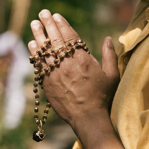 Gold plated rudraksha bead necklace held in praying hands, devotional lifestyle shot