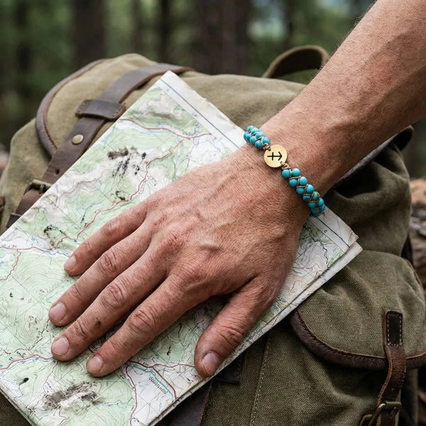 Turquoise Sagittarius zodiac bracelet worn on a man's wrist over a trail map, gold sign charm on top