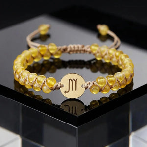 Close-up of glossy yellow citrine beads and gold Scorpio charm on the woven zodiac energy bracelet